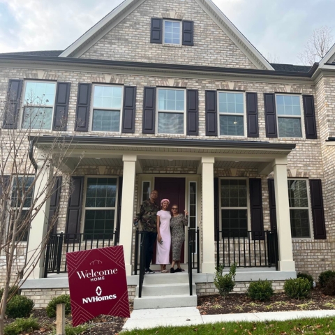 New homeowner posing in front of modern NVHomes property with 'Welcome Home NVHomes' sign
