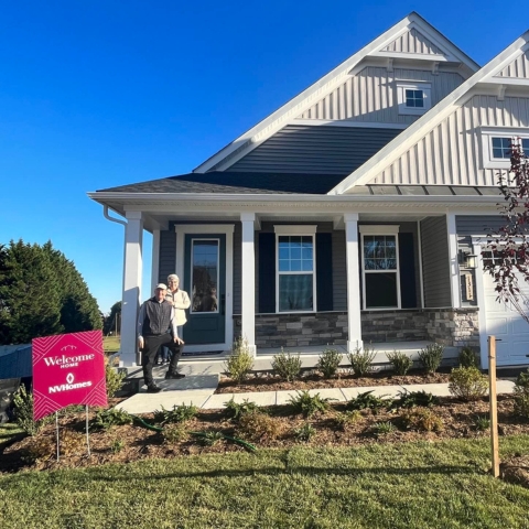 Family celebrating new home purchase with with large red '#NVHomes' key sign