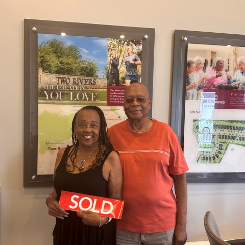 couple celebrating home purchase at NVHomes Two Rivers community, holding red 'SOLD' sign