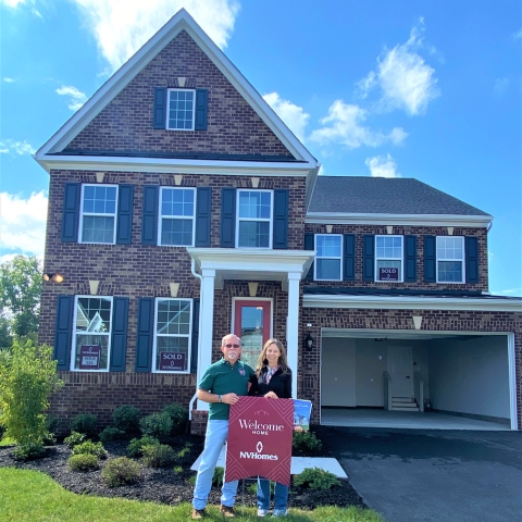 Couple celebrating new home purchase in front of two-story brick NVHomes property