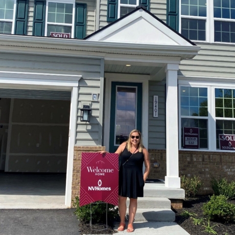 New homeowners posing in front of NVHomes property with 'Welcome Home NVHomes' sign